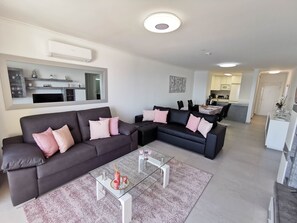 A modern living room with two dark sofas, a glass coffee table, and a kitchen in the background. - Flat Rose Garden Sea View (Portimão)