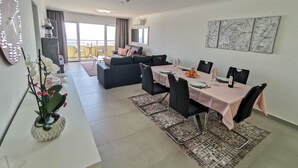 A modern dining area with a table set for four, a sofa, and a balcony with a view. - Flat Rose Garden Sea View (Portimão)