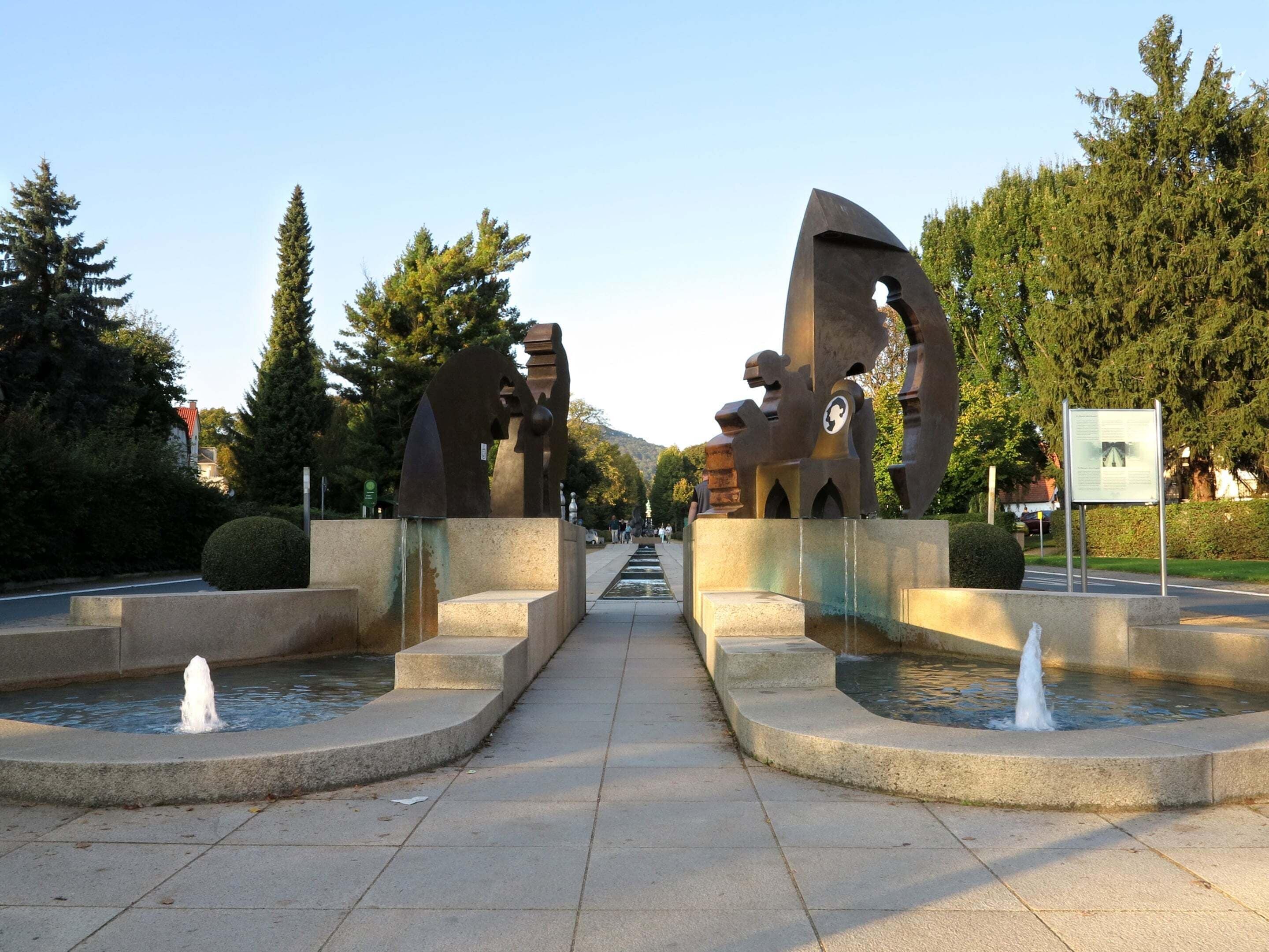 A public park with abstract sculptures, a fountain, and a paved walkway.