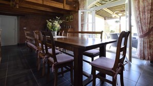 A rustic dining area with a wooden table and chairs, a vase of flowers, and a view of the outside through a glass door.