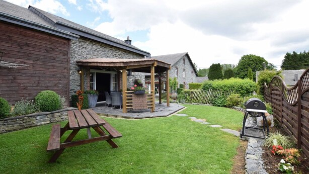 A rustic house with a stone exterior, a wooden deck, and a thatched-roof outdoor seating area.
