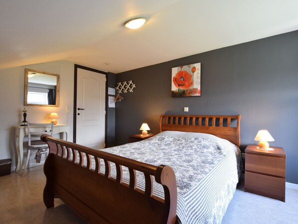 Une chambre avec un lit en bois, des tables de chevet avec des lampes, un bureau avec une chaise, un miroir et un mur orné d’un tableau représentant des coquelicots.