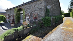 A stone building with a sloped roof, a small porch, and a sign that reads "Mouillac Gîte."