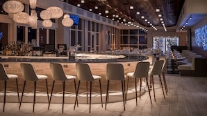 Zona de bar moderna amb una barra central, diverses disposicions d'seients i un sostre de fusta amb llums penjants.