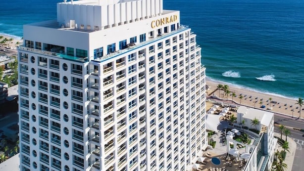 Un hotel modern i alt amb un prominent cartell de "CONRAD", nombrosos balcons i vista a l'oceà.