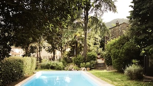 A rectangular swimming pool with two lounge chairs in the foreground.