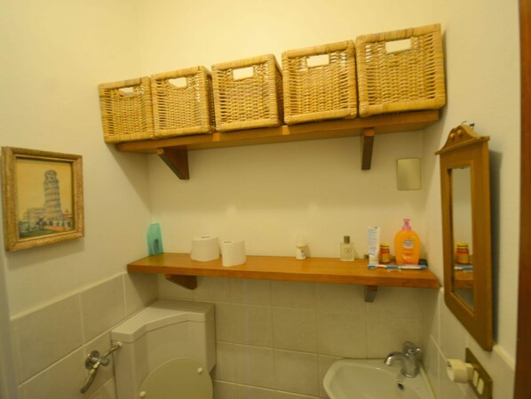 A bathroom with a toilet, sink, and a wooden shelf above holding baskets.