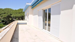 A building with a tiled balcony, white shutters, and a view of a forested hill. - Villa in Vilamoura With Private Pool & BBQ (Loulé)