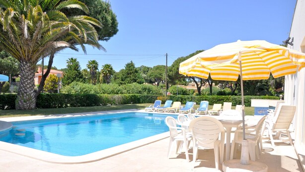 A swimming pool with lounge chairs and a table, surrounded by palm trees and greenery. - Villa in Vilamoura With Private Pool & BBQ (Loulé)