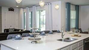 Une cuisine moderne dotée d’un îlot central, d’appareils électroménagers en acier inoxydable et de luminaires suspendus.