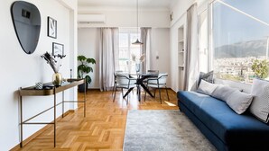 Una sala moderna con un sofá azul, una mesa de comedor con sillas, un ventanal con vista a la ciudad y piso de madera.
