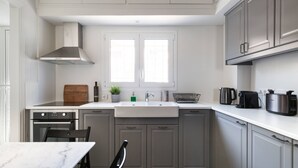 Una cocina moderna con encimera blanca, armarios grises, horno integrado, un lavamanos y un ventanal sobre el fregadero.
