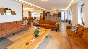 Uma sala de estar moderna com dois sofás marrons, uma mesa de centro de madeira e uma cozinha ao fundo.