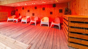 Sala de sauna com paredes, teto e chão de madeira. Seis cadeiras brancas dispostas em duas fileiras.