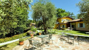 A yellow villa with a stone patio, outdoor seating, and lush greenery. - Belvilla by OYO Bilo del Ruscello (Manerba del Garda)