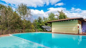 A clear blue swimming pool with a tiled deck, surrounded by trees and a building with a tiled roof. - Belvilla by OYO Bilo del Ruscello (Manerba del Garda)
