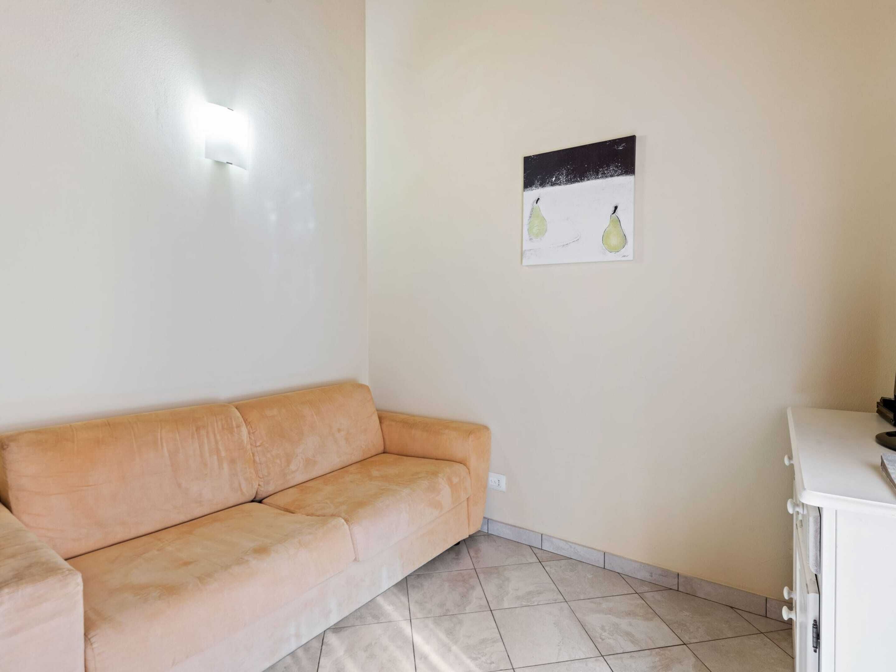 A room with a beige sofa, a white cabinet, and a wall-mounted picture of pears.