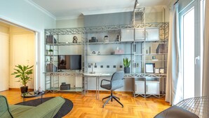 A modern, open-plan living space with a wooden herringbone floor, a central desk area with a computer and shelves, and a seating area with a green sofa and a black chair. - Superb 1BD Apartment in the heart of Kolonaki (Athens)