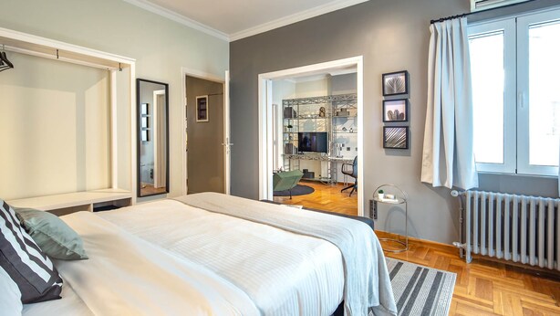 A bedroom with a large bed, a walk-in closet, and a view of a kitchen area. - Superb 1BD Apartment in the heart of Kolonaki (Athens)