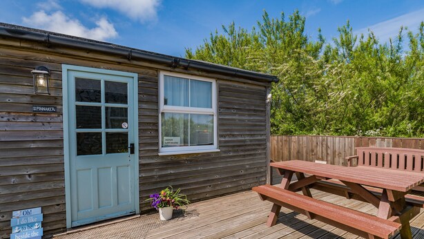 A wooden cabin with a door, a window, a sign, a bench, and a small potted plant. - 2 bedroom accommodation in Staithes, near Whitby (Staithes, near Whitby)