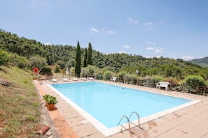 A rectangular swimming pool with a tiled deck, surrounded by lounge chairs and potted plants.