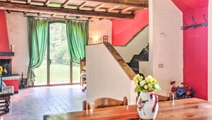 Un espace repas avec une table en bois, des rideaux verts, un escalier et une vue sur l’extérieur.
