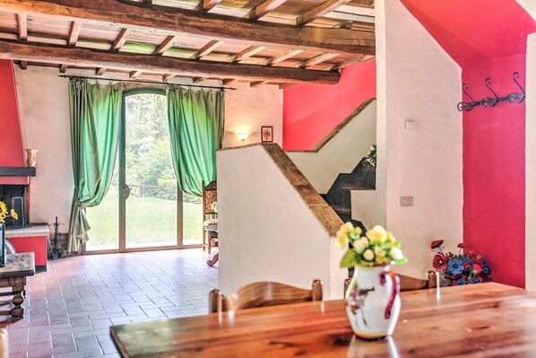 A dining area with a wooden table, green curtains, a staircase, and a view of the outdoors.