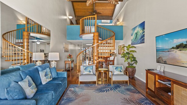 Ein großzügiger Wohnbereich mit einem blauen Sofa, einer Wendeltreppe aus Holz und einem großen Flachbildfernseher.