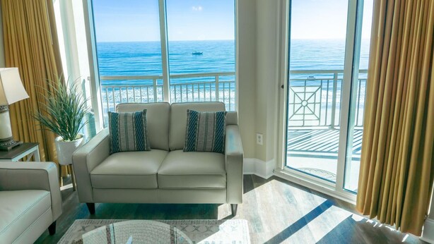 A living room with a sofa, a lamp, and a view of the ocean through large windows. - MVG 1111 3 Bedroom 3 Bath Oceanfront (North Myrtle Beach)