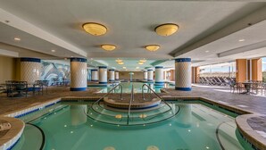 A large indoor swimming pool with multiple lanes, surrounded by lounge chairs and tables, and featuring a checkered column design. - MVG 1111 3 Bedroom 3 Bath Oceanfront (North Myrtle Beach)