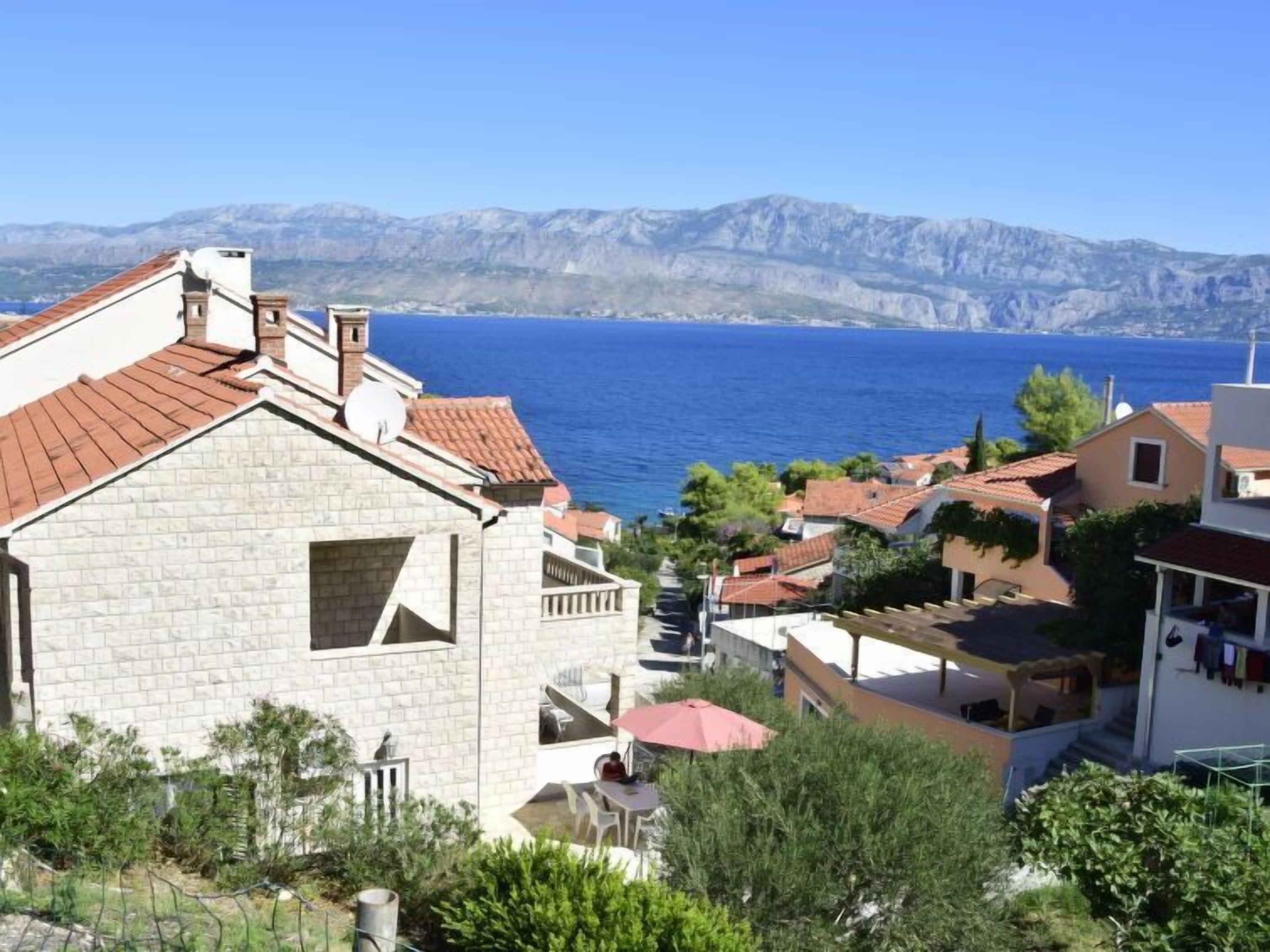 A coastal village with stone buildings, a clear view of the sea, and a mountainous backdrop.