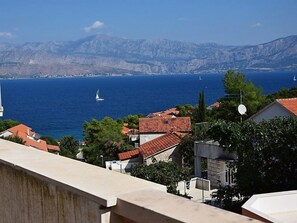 Un pueblo costero con edificios de tejados rojos, un mar azul cristalino y montañas al fondo.