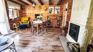 A cozy log cabin interior with a dining area, yellow armchair, fireplace, and wooden walls.