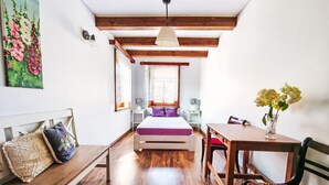 A bedroom with a wooden bed, a wooden desk, a chair, a bench, and a vase with flowers.