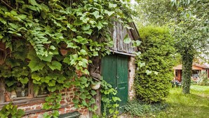 A rustic brick building with a green door, overgrown with ivy, and a small wooden bench at the entrance.