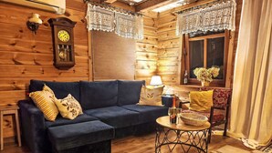 A cozy log cabin interior with a dark blue sofa, a wooden floor, a round metal table with drinks, and a dog lying on the floor.