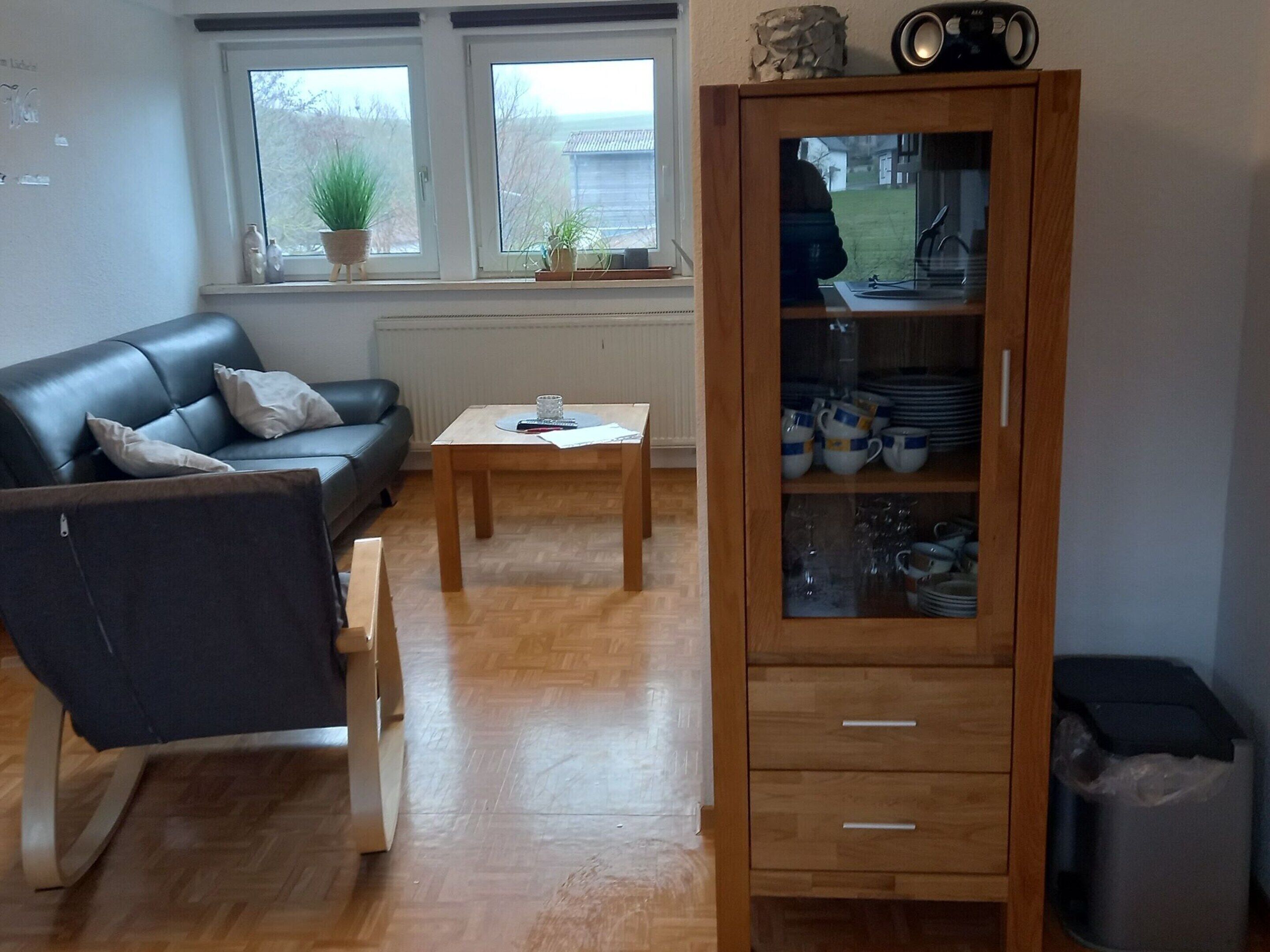 Olohuone, jossa on sohva, sohvapöytä ja astioita sisältävä kaappi.