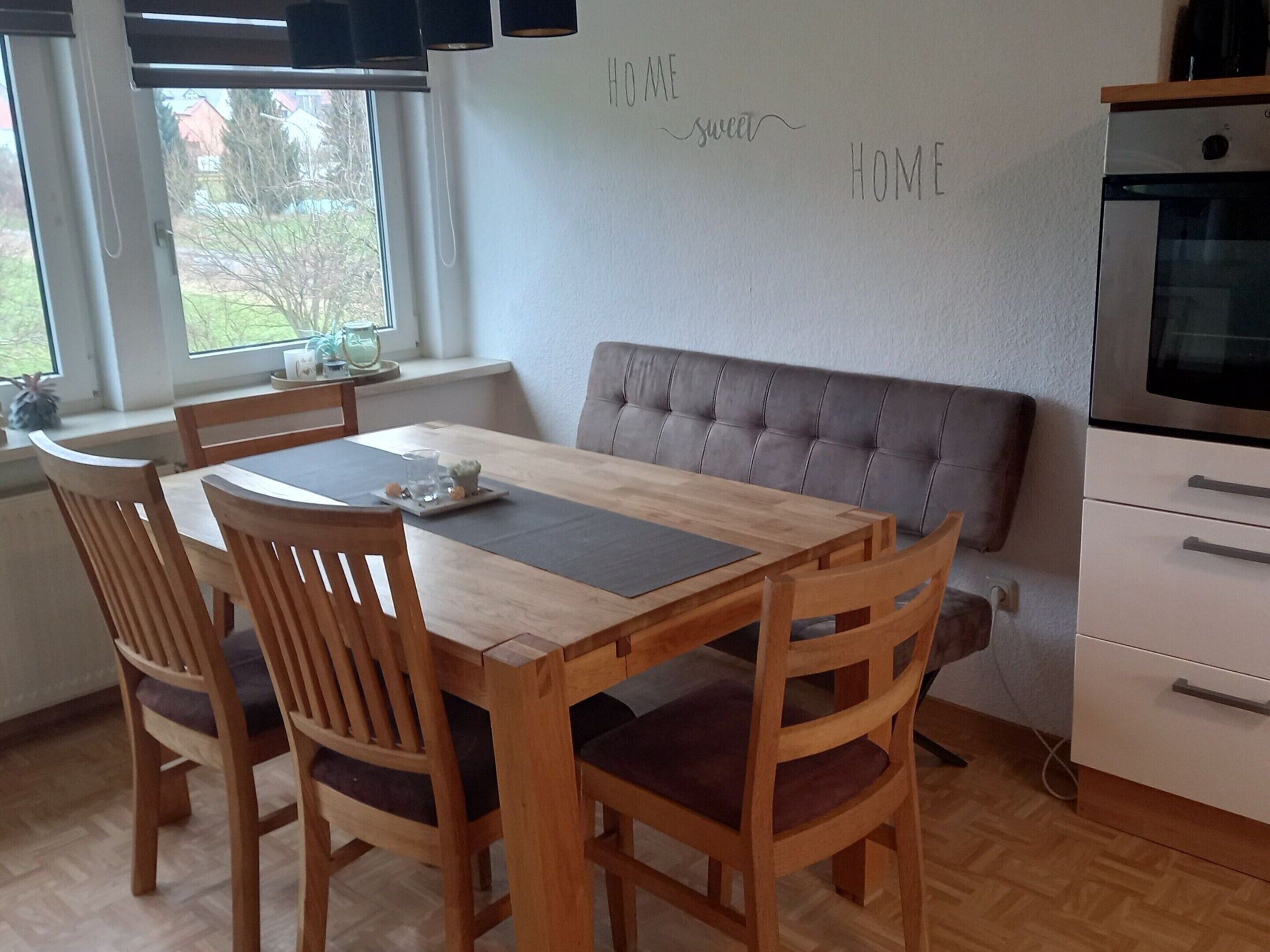 A dining area with a wooden table and chairs, a bench, and a kitchen area with a stove and cabinets.