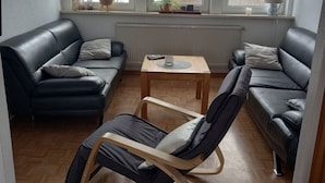 Ein modernes Wohnzimmer mit zwei schwarzen Ledersofas, einem Holztisch und einem Schaukelstuhl.