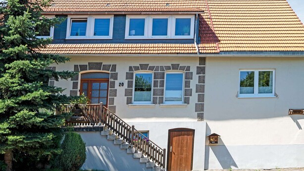 Ein zweistöckiges Haus mit Ziegeldach, Steinverzierungen und einer Holztreppe zum Eingang.