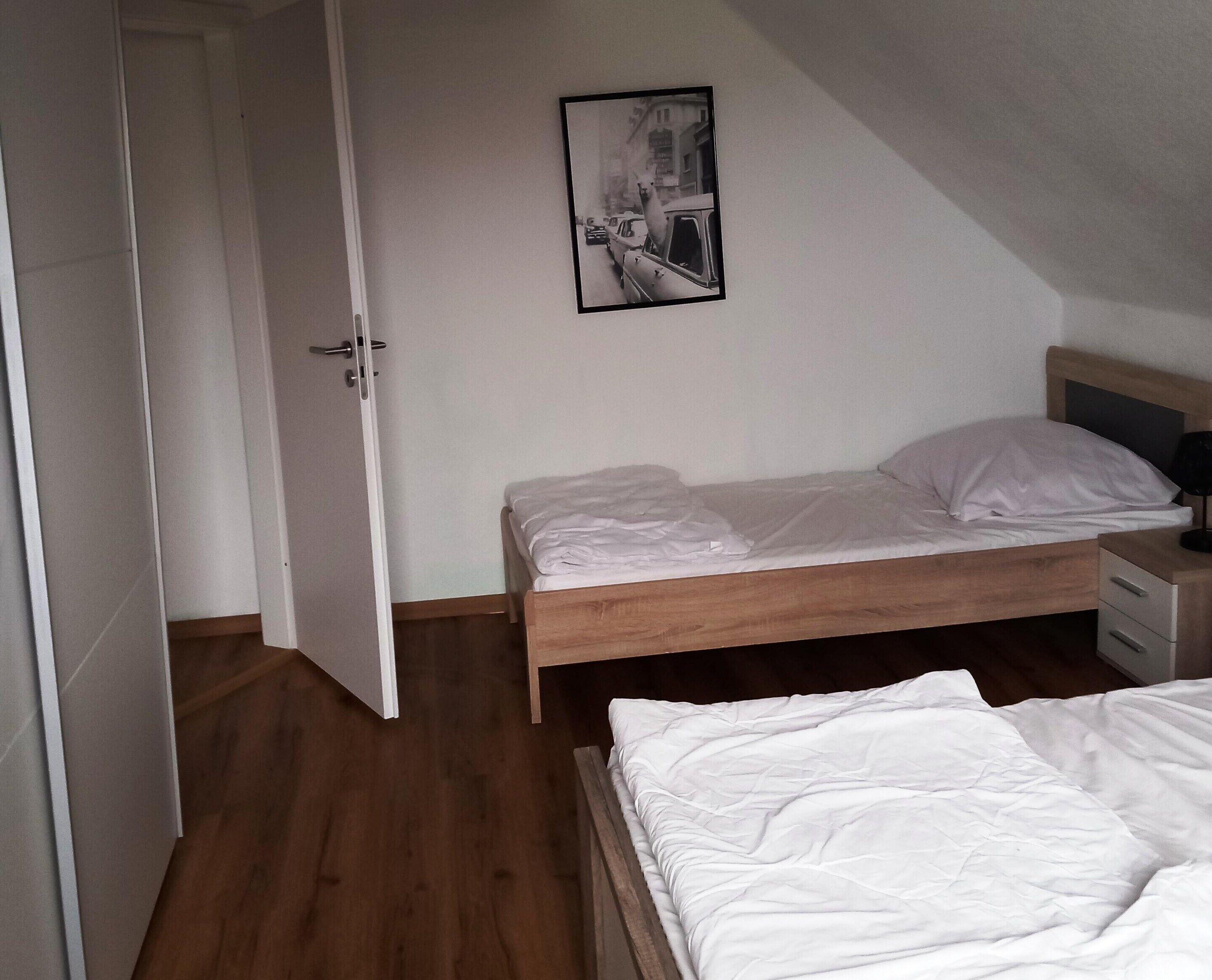 Un dormitorio con cama de madera, colchón blanco y mesita de noche con lámpara.