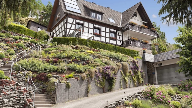 A traditional half-timbered house with a sloped roof, a stone staircase, and a lush garden. - Gemutliches Appartement in Hallenberg mit Terrasse (Hallenberg)