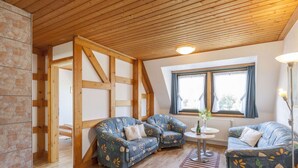 A cozy room with wooden beams, a stone wall, and two sofas with floral upholstery. - Gemutliches Appartement in Hallenberg mit Terrasse (Hallenberg)