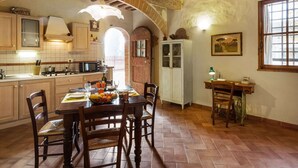 A rustic kitchen with exposed wooden beams, a tiled floor, and a dining area with a table set for two. - Belvilla by OYO Archi (Monteroni d'Arbia)