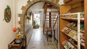 A hallway with a stone archway, a wooden staircase, a small table with flowers, and a bookshelf filled with magazines. - Group Cottage in Lierneux (Lierneux)