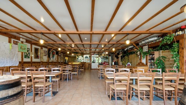 A restaurant with wooden tables and chairs, a tiled floor, and a ceiling with wooden beams and hanging lights. - Group Cottage in Lierneux (Lierneux)