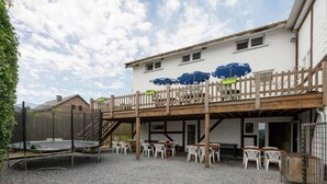 A covered outdoor seating area with tables and chairs, a trampoline, and a wooden deck with umbrellas. - Group Cottage in Lierneux (Lierneux)