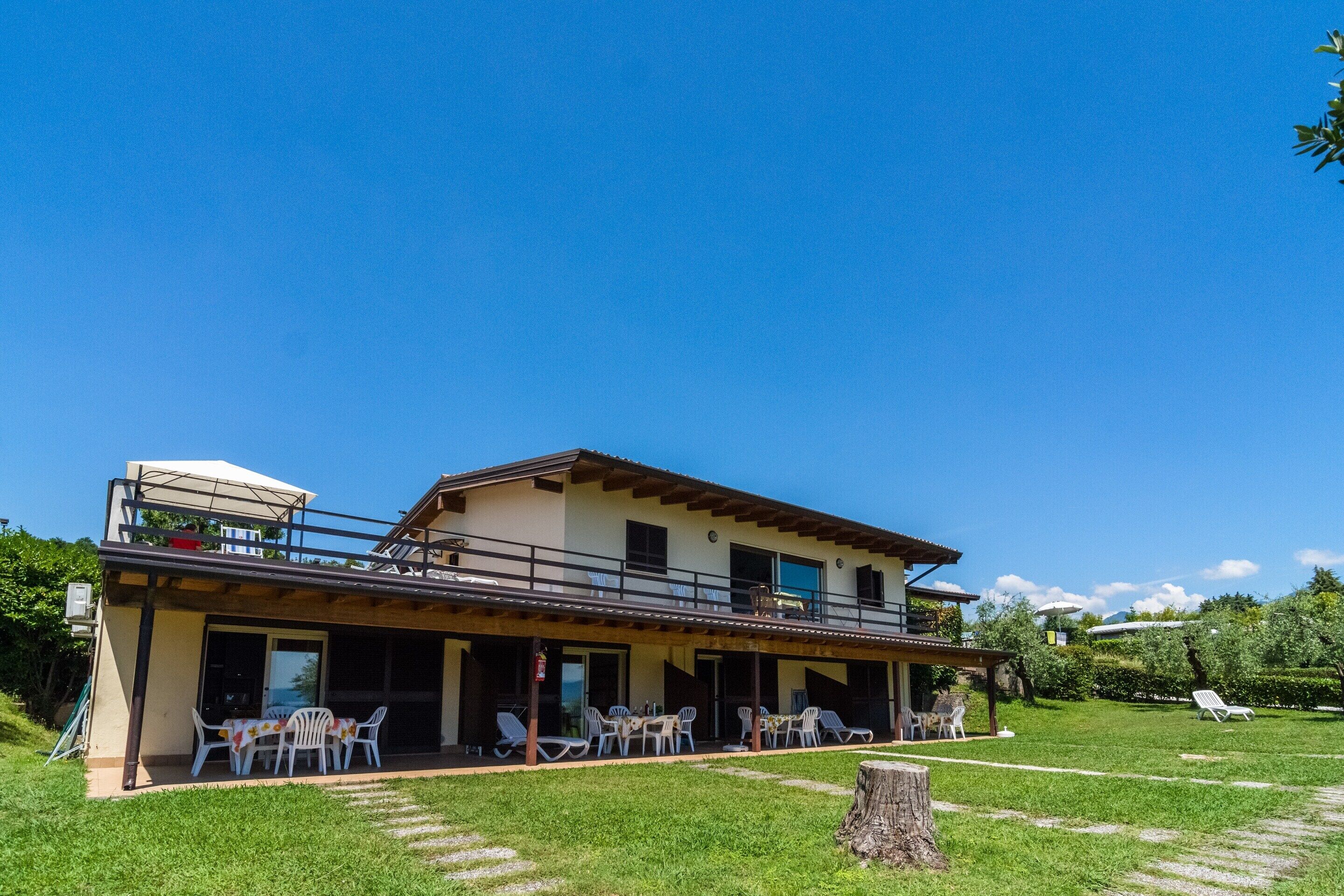 A two-story building with a covered patio area, outdoor seating, and a grassy lawn.