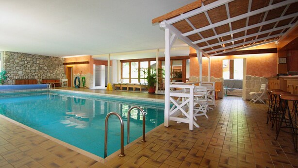 Ein Innenpool mit Steinwand, Holzterrasse und überdachtem Sitzbereich.