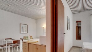 Ein kompakter Raum mit Küchenzeile, einer Essecke mit Tisch und Stühlen, einem Bett und einem kleinen Fenster.